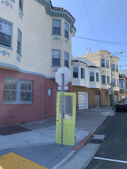 a yellowish-green door stands on the sidewalk leaning on a stop sign