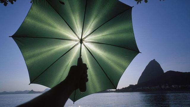 The sun is low above a lake. You can see the silhouette of someone's arm holding an umbrella in front of the sun.