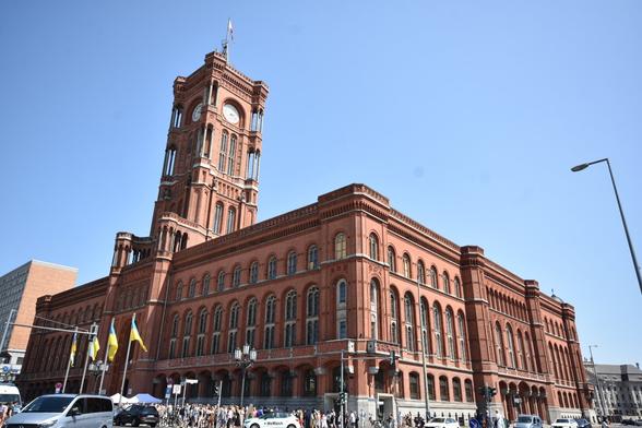 Full view of the Roten Rathaus in Berlin. it is a characteristic 3 floor red building with a tower. Here, 2 sides of the building and the tower with the Berlin flag on top of it are visible