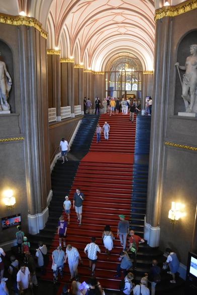 View from the first floor of the main stairs inside the Rathaus. The stairs have a red carpet, while each side of the hall has a statue