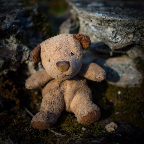 Ein kleiner Teddy (nur wenige cm gro0) sitzt auf einer alten verwitterten Steinmauer.