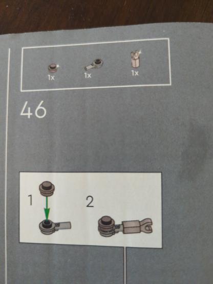 Photo of a Lego instruction book page showing three pieces across the top and then the steps to put them together. In the top area, two of the pieces have a little tiny dot of sparkle to notate chrome color. In the actual instructions, the pieces are shown as a grey color.