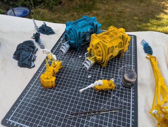A wider shot of the two Plasma Generatorium on a cutting mat along with some additional terrain features around. There's two engines and a crane assembly in Iron Fists yellow as well as some scatter terrain of fallen statues, mostly blocked out in a mix of Akhelian Green and Leviadon Blue before I dry-brush them bronze and add some verdigris. All the metalwork still needs to be done.