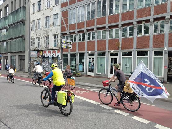 Ein Fahrradfahrer bei der Fahrradsternfahrt Hamburg mit einer großen weißen Fahne auf der ein rot durchgestrichenes Verkehrsschild Autobahn A20 ist.