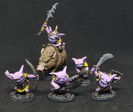 5 minis, 4 on foot, one riding a brown boar. All are squat humanoids with squinty eyes, broad mouths, and big ears. They have pink skin, yellow tunics, and a variety of weapons.