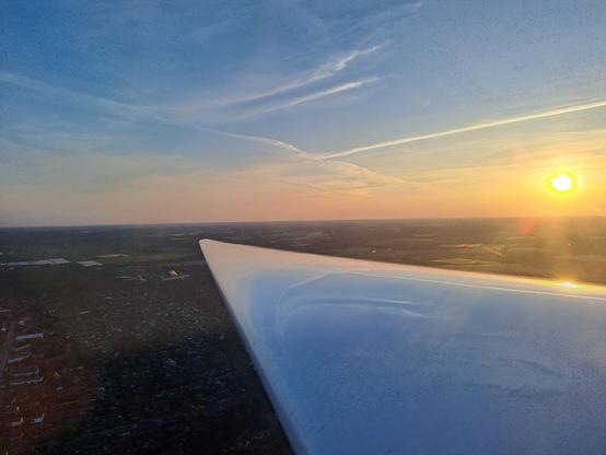 Foto aus der Luft, diesmal über die rechte Tragfläche auf die gleiche Ortschaft. Die Sonne steht rechts im Bild über dem Horizont.