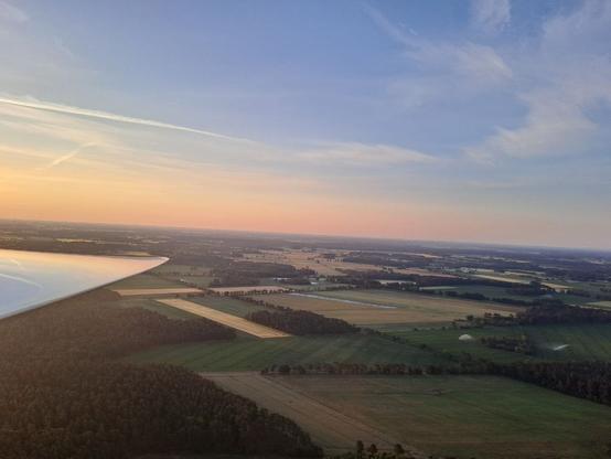 Foto aus der Luft mit der Sonne im Rücken. Dadurch sieht man die Felder und Waldstücke am Boden viel klarer und es wirkt alles noch etwas weniger hell.