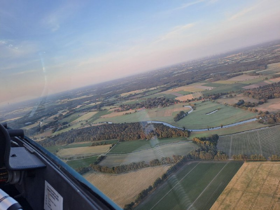 Foto während des Windenstarts. Man sieht den Horizont schräg wegen der eigenen steilen Lage im Start. Ein Fluss schlängelt sich durch Felder und Waldstücke.