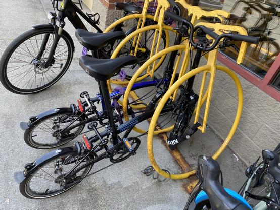 two brompton folding bicycles, one blue and one black, in the upper rack at lake forest park town centre