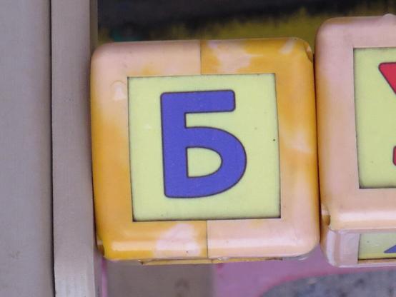Синяя буква Б на грани жёлтого пластикового кубика. // Blue letter Б (Cyrillic B) on the edge of a yellow plastic cube.