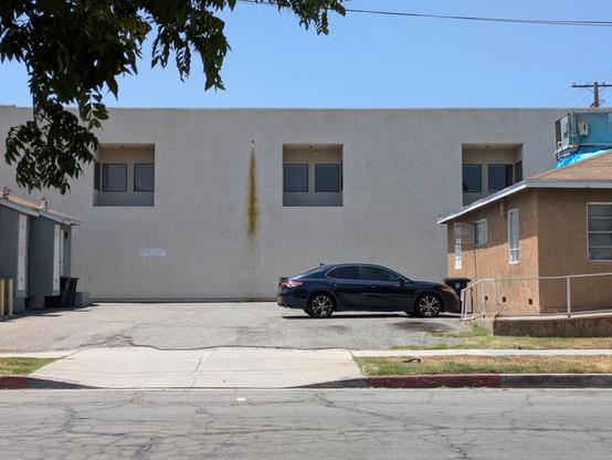 A two-story, flat, white building exterior with recessed pairs of windows. A rusty brown streak runs down the wall to the left of the middle window.