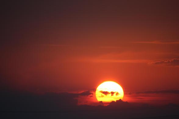 Sonnenuntergang. Die Sonne als hellleuchtender Ball von dem nur noch 2/3 zu sehen ist. Der Himmel ist rot gefärbt, ein paar Wölkchen sind im Bild verteilt.
Matzework