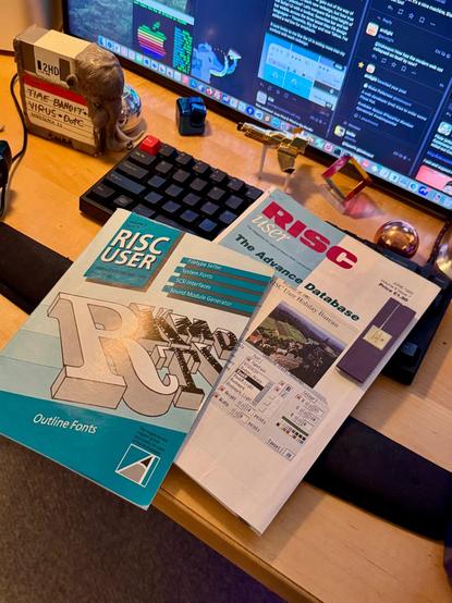 Two RISC User magazines lying on a desk, on the keyboard of a computer setup
