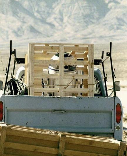 picture of R2-D2 in a giant crate in the back of an old ratty ford pick-up truck in the middle of the desert.