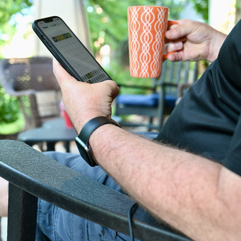 My self portrait holding a coffee cup in one hand and a phone with Wordle in the other hand.