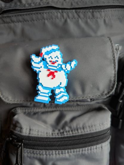 3d printed pin of a pixel art Stay Puft from Ghostbusters pinned to a courier bag.