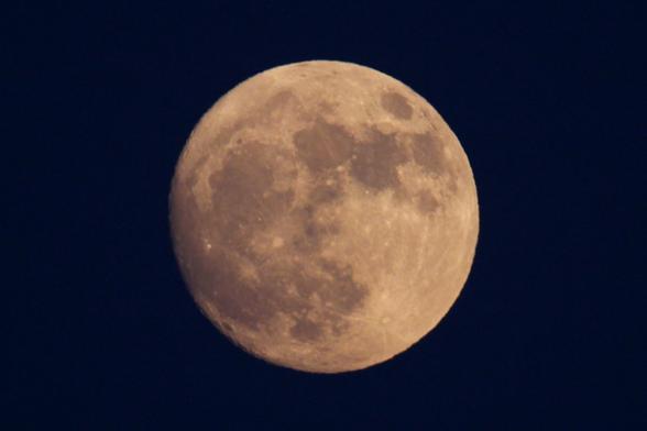 Image of a nearly full Moon against a dark blue sky. This June moon from 9:31 pm EDT on June 9 is just 30 hours short of being completely full. The edges of the left and lower left show the small hint of shadow and definition on the edges of craters where it is not yet completely full.