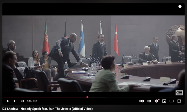 screenshot of men in suits fighting around a giant round table