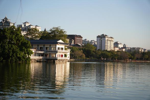 A pagoda-like house facing the sea, similar buildings can be seen in the distance. There are many trees on the coast. The afternoon sun shines on the house.