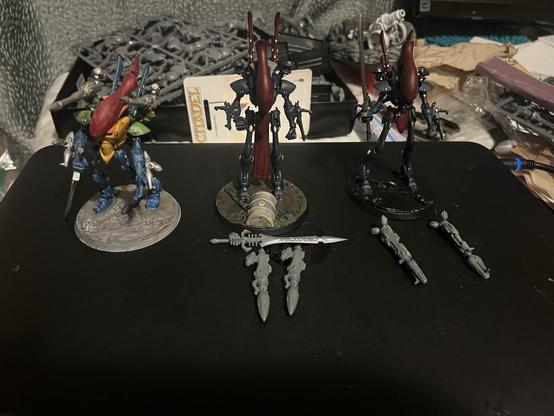 Warhammer 40K miniatures. 

Three wraith lords. 

One finished, with rainbow colors and twin bright lances. 

Two unfinished, painted dark red and dark blue. Two star cannons, a sword in fist, and two missile launchers unpainted in front of them.
