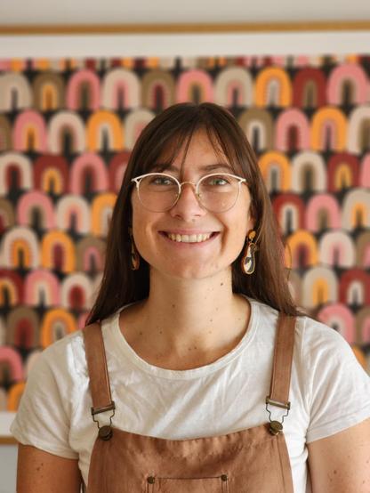 Front-facing photo of Alise Fox, with a big smile on, in front of a colourful artwork.