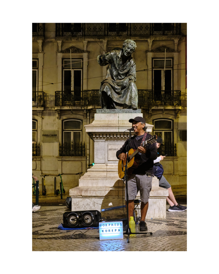 singer orpheus kurepa performing with his guitar and joy in front of statue of antónio ribeiro in lisbon by night, his name on a lightbox nearby