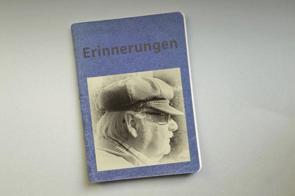 Das Bild zeigt ein blaues Notizbuch, das mit einem Bild von Oppa Ömmes und dem Text "Erinnerungen" beschriftet ist.