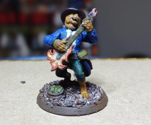 A catfolk miniature in a long coat and hat playing a fire-shaped guitar and bearing other instruments on his body. A bag of coins is on the ground at his feet