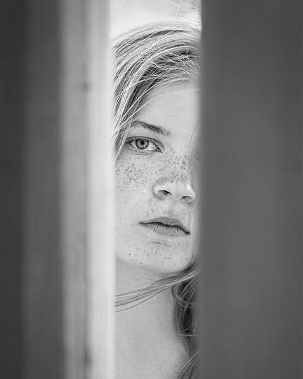 Portrait eines 15jährigen Mädchens mit Sommersprossen, das hinter zwei Säulen steht, die das Gesicht zu 1/3 verdecken.