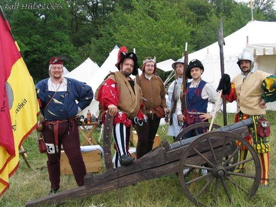 A group of men in pesudo-historical costumes are assembled around a fake cannon