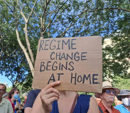 A demonstrator carrying a sign that reads "Regime change begins at home."