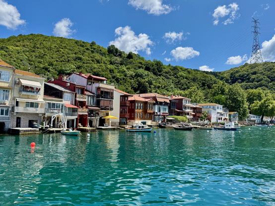 Boats on a green sea with traditional wooden houses, blue sky and lush green hills