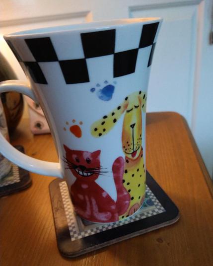 Large mug of tea on a bedside cabinet with a checkerboard pattern at the top.
A large yellow dog is on the right and a small red cat on the left