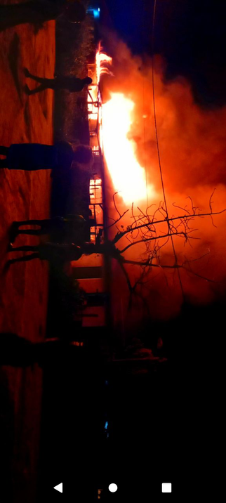 The image depicts a nighttime scene with a large fire burning intensely in the background. The fire is bright orange and yellow, illuminating the surrounding area and casting a glow on the nearby structures. Thick smoke is rising from the fire, creating a hazy atmosphere. In the foreground, several silhouetted figures are standing, observing the fire. The ground appears to be a dirt surface, and there are bare tree branches in the foreground, adding to the starkness of the scene. The fire is consuming a building, with flames visible through the windows and around the structure. The overall scene is chaotic and dramatic, with the fire being the central focus.

Provided by @altbot, generated privately and locally using Ovis2-8B

🌱 Energy used: 0.699 Wh