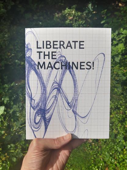 A hand holds up a copy of a book entitled "Liberate The Machines!". The cover depicts a complex graph on graph paper.