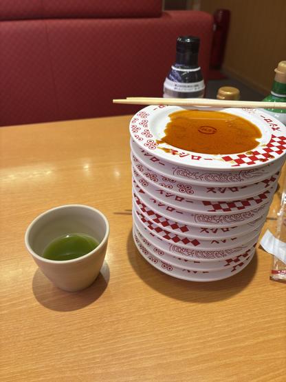 A stack of 10 small sushi plates, with chopsticks on top and a green tea at the side