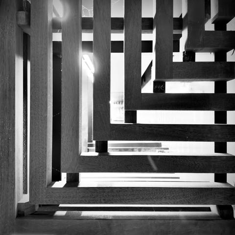A wooden support structure is viewed in black and white, as its beams ascend in right angles from the bottom-left of the frame to the top-right.