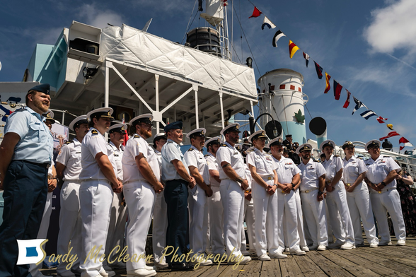 Group shot of Navy sailors in uniform in front of an historic warship.
