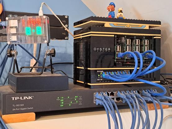 An Ethernet switch, with #RaspberryPi computers stood on it. One has a 16x16 LED display and a 2 Terabyte hard disc. On the right is a cluster of four Raspberry Pi 3s, in a case built of #Lego.