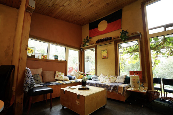 photo from google maps: an interior photo of a 4m x 4m room inside the SOURCE building, the space currently used to hold GRANT meetings in. cushioned seating borders the wall, an aboriginal flag pinned on the wall, sunlight shines on the garden outside the window