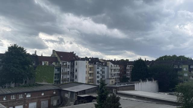 View of a backyard surrounded by apartment blocks. The sky is darkened by a large, dark cloud