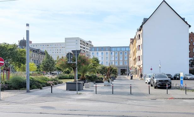 Die Eichenstraße nachher. Auf dem ehemaligen Parkstreifen an der Straße stehen jetzt viele große Pflanzen in Töpfen, Sitzgelegenheiten und Radabstellmöglichkeiten.