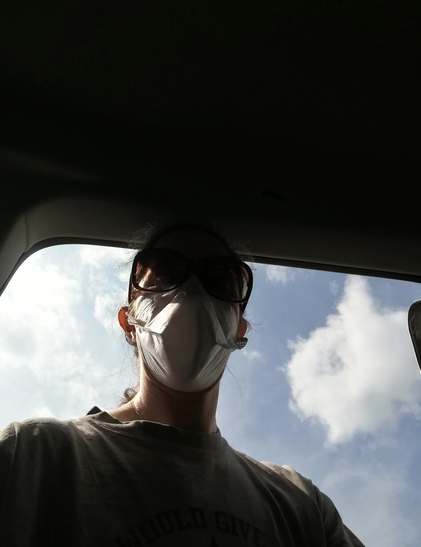 Selfie of a me wearing a duckbill respirator and sunglasses. Not a lot else of me is visible because the pale blue sky with some soft clouds is too bright and I didn't adjust the exposure. I am framed by a car door.