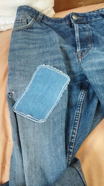 Patch thermocollant en toile de nîmes cousus au fil clair aux bords sur mon jeans bleu. Le tout posé sur un drap orangé