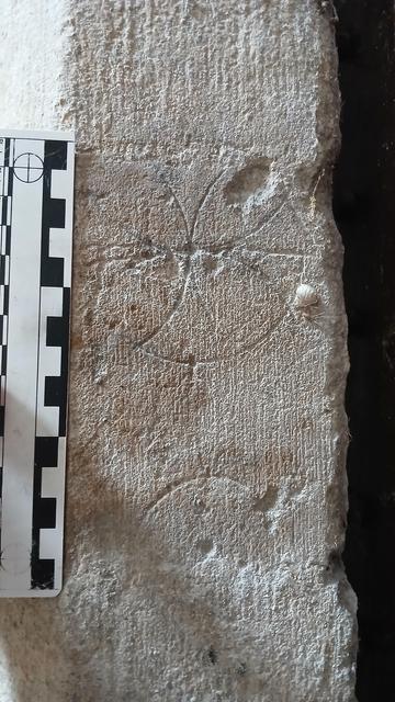 Two marks made with a compass in a medieval doorframe the upper a quatrefoil, the lower a circle. A photographic scale on the left.