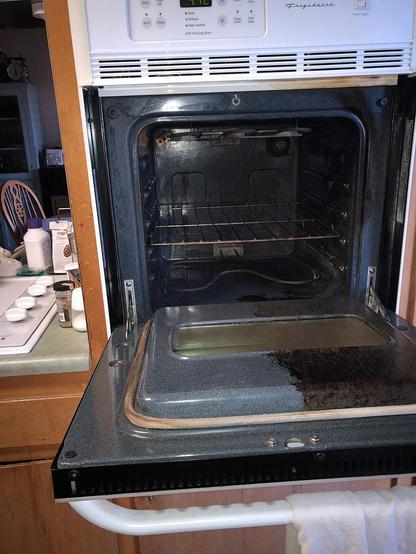 From 2018 old oven opened to show half the inside oven door cleaned from many years of dark, baked-on grease. It is very stark to see the shiny light gray enamel next to the dirty dark brown enamel to the right. Used non-toxic enzyme oven cleaner as described in post.