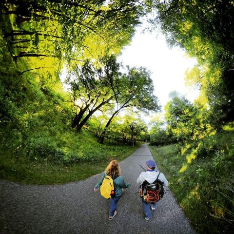 One of a series of photographs in which two people are pictured hiking, biking, and kayaking throughout a beautiful and verdant state park in central Minnesota under cloudy blue late-summer skies.