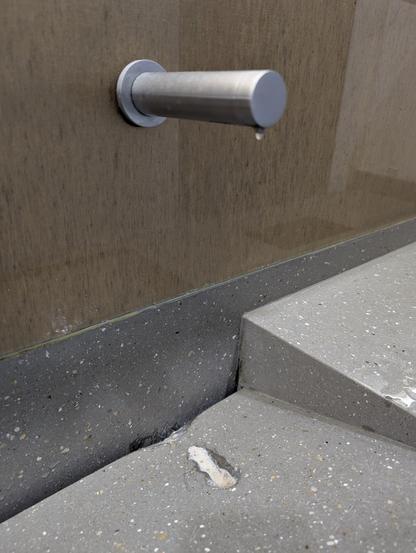 A soap dispenser mounted above a sink, underneath it the sink has been eroded into a deep groove