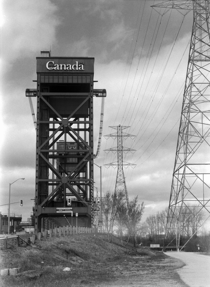 The lift bridge at the entrance to Hamilton Harbour stands starkly against a cloudy sky alongside power transmission pylons.