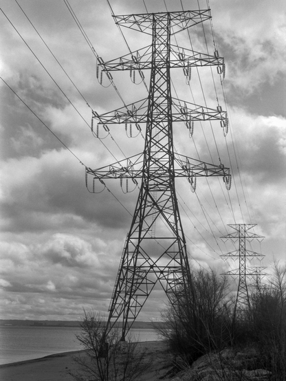 A row of power transmission pylons line the beach.